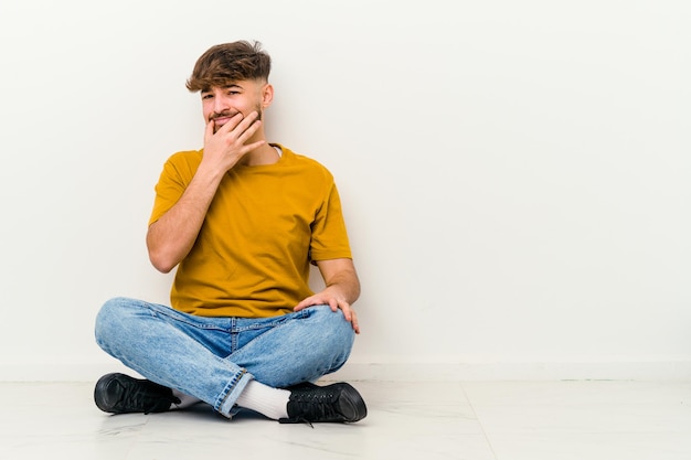 Jonge Marokkaanse man zittend op de vloer geïsoleerd op wit twijfelen tussen twee opties.