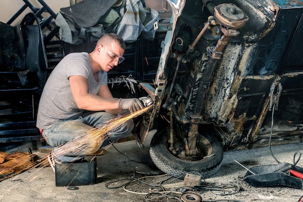 Jonge mechanische arbeider die een oude carrosserie van een oldtimer repareert in een rommelige garage