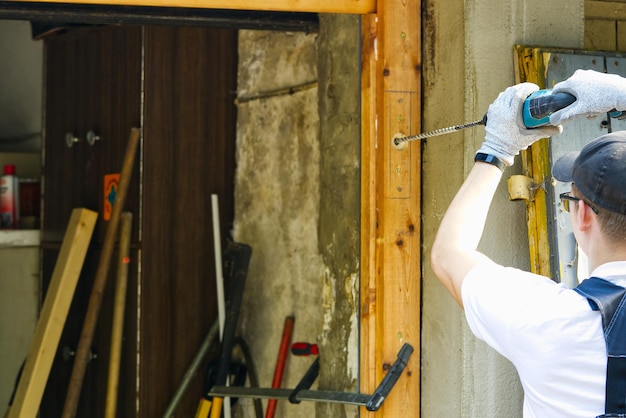 Jonge meester die het oude klusjesman van garagedeuren herstelt die een rot houten gebouw herstelt