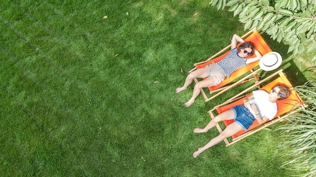 Jonge meisjes ontspannen in de zomertuin in ligstoelen op gras op gras, vriendinnen hebben plezier buitenshuis