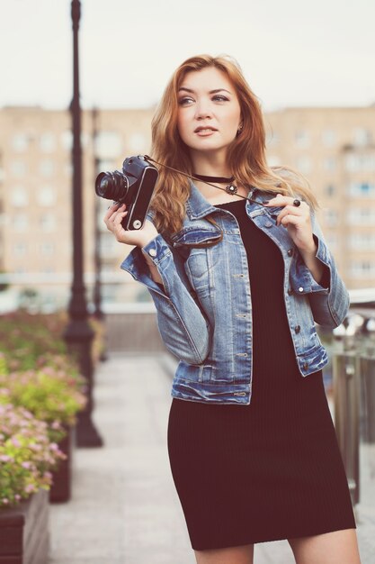 Jonge meisjesfotograaf die langs de straat loopt in een spijkerjasje met een oude camera