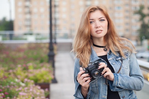 Jonge meisjesfotograaf die langs de straat loopt in een spijkerjasje met een oude camera