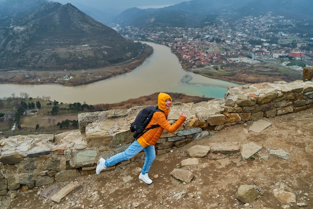 Jonge meisjestoerist verheugt zich over het poseren tegen de achtergrond van een verbazingwekkend natuurlijk landschap. De samenvloeiing van twee rivieren in de stad Mtscheta in Georgië.