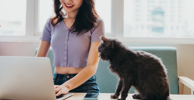 Jonge meisjeszitting die aan bank en kattenzitting naast laptop werkt