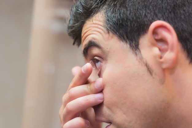 Jonge mens die contactlens in zijn oog zet