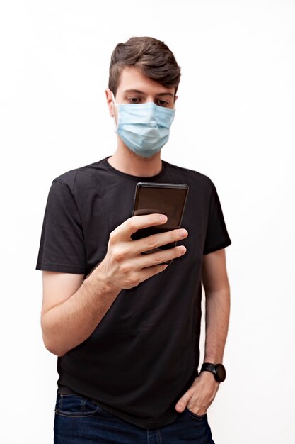 Jonge mens die een gezichtsmasker draagt dat zijn mobiele telefoon controleert