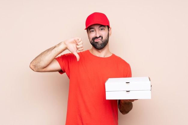 Jonge mens die een pizza over geïsoleerde tonende duim houdt