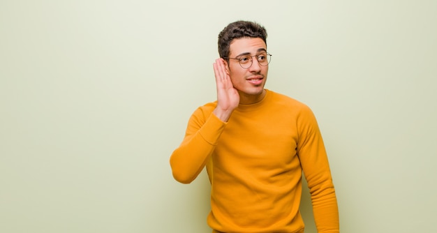 Jonge mens die ernstig en nieuwsgierig kijkt, luisterend, proberend om een geheim gesprek of roddel te horen, afluisterend over muur