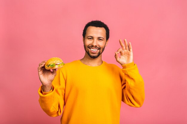 Jonge mens die hamburger eet die over roze wordt geïsoleerd