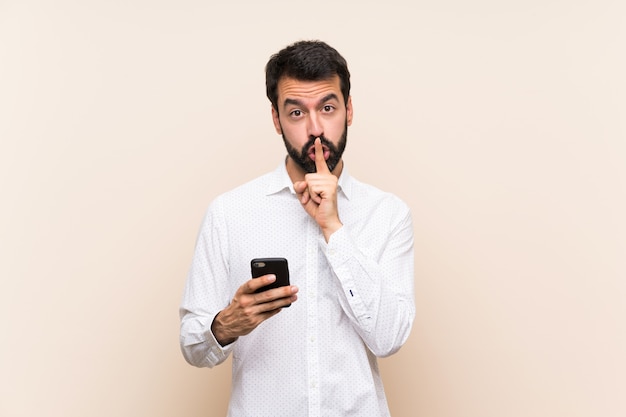 Jonge mens die met baard mobiel houden die een teken van stiltegebaar tonen die vinger in mond zetten