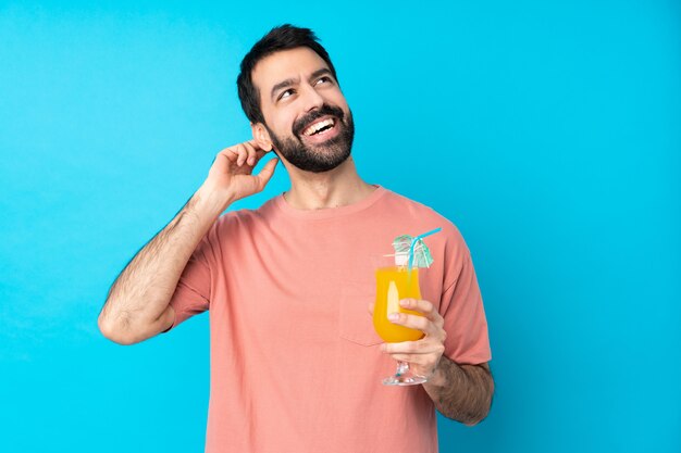 Jonge mens die over een cocktail over geïsoleerde blauwe muur houdt die een idee denkt