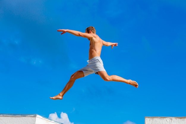 Jonge mens die parkour sprong op de blauwe hemelachtergrond doet op zonnige de zomerdag