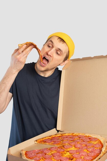 Jonge mens die pizza eet met een doos in zijn handen
