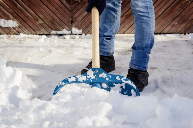 Jonge mens die sneeuw op de oprijlaan scheppen dichtbij de garage