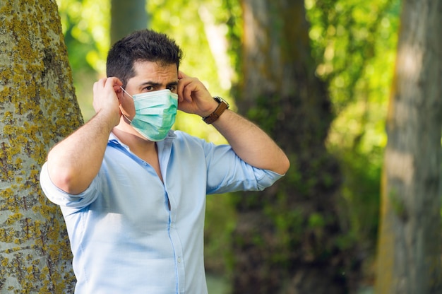 Jonge mens die zich in het park bevinden die beschermend gezichtsmasker verwijderen die overwinning over coronavirus buiten in openlucht vieren. Einde van quarantaine. Masker verwijderen. Buitenshuis. Vrijheid. Covid19. Pandemische crisis is voorbij.