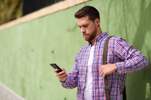 Jonge mens die zijn slimme telefoon op stedelijke achtergrond kijkt. Levensstijl concept.