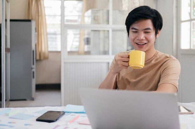 Jonge mens het ontspannen met een kop van koffie en thuis het gebruiken van computerlaptop