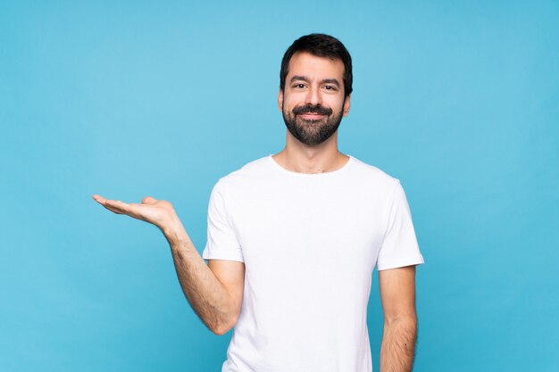 Jonge mens met baard over geïsoleerde blauwe achtergrond die copyspace denkbeeldig op de palm houden om een advertentie op te nemen