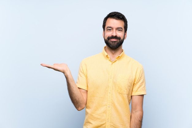 Jonge mens met baard over geïsoleerde blauwe muur die copyspace denkbeeldig op de palm houden om een advertentie op te nemen