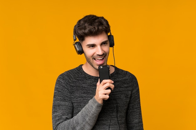 Jonge mens over geïsoleerd gebruikend mobiel met hoofdtelefoons en het zingen