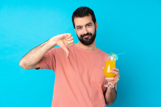 Jonge mens over het houden van een cocktail over geïsoleerde blauwe muur die duim toont