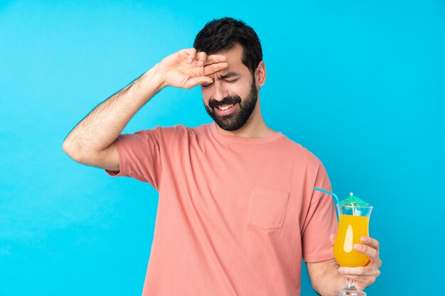 Jonge mens over het houden van een cocktail over geïsoleerde blauwe muur met vermoeide en zieke uitdrukking