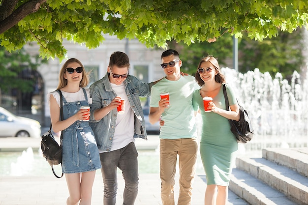 Jonge mensen die door de stad lopen. Stijlvolle vrienden die samen plezier hebben. Groep mensen koffie drinken en praten.