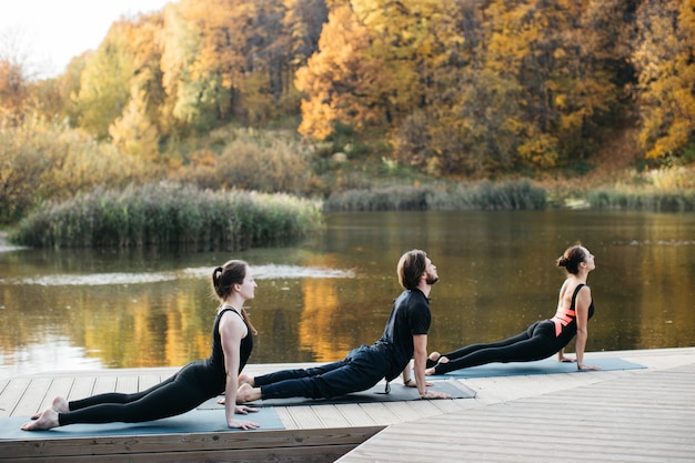 Jonge mensen doen yoga asana in de natuur in de buurt van het meer