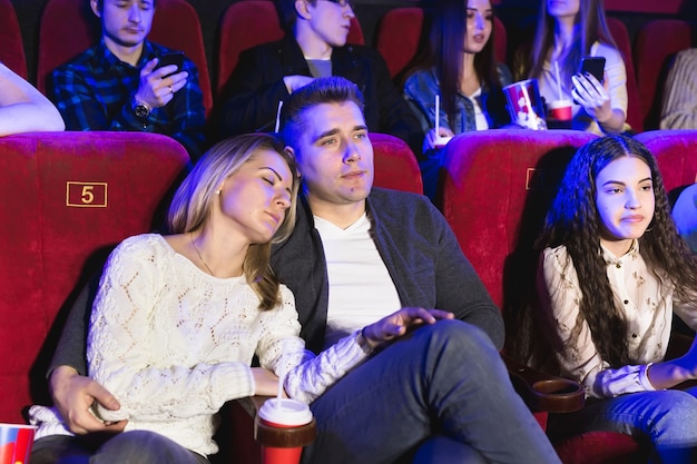 Jonge mensen kijken naar een saaie film in de bioscoop, vrouw slaapt
