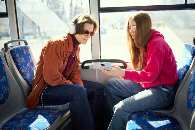 Jonge mensen positieve man en vrouw die gebruik maken van het openbaar vervoer tram en kijken op mobiele telefoon