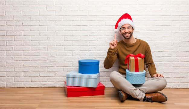 Jonge mensenzitting met giften die kerstmis vieren die nummer één tonen