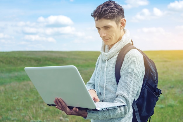 Jonge mensenzitting op een groene weide met laptop draadloze, blauwe bewolkte hemel