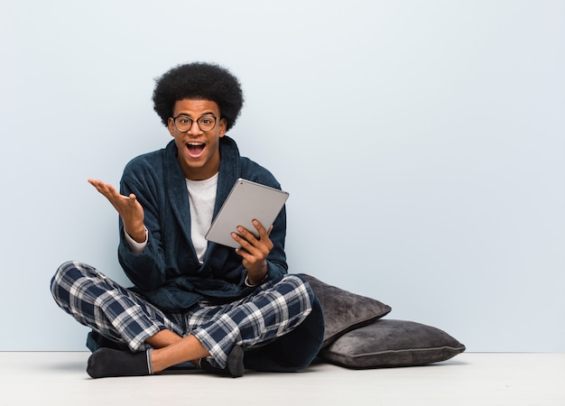 Jonge mensenzitting op zijn huis en holding zijn tablet die een overwinning of een succes vieren