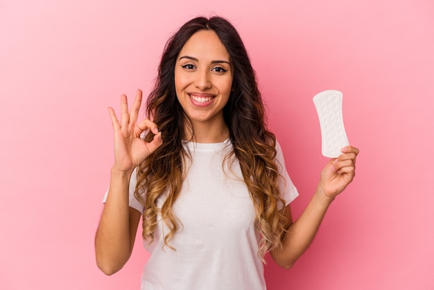 Jonge Mexicaanse vrouw die een kompres houdt dat op roze muur wordt geïsoleerd vrolijk en zelfverzekerd tonend ok gebaar.