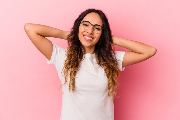 Jonge Mexicaanse vrouw die op roze muur wordt geïsoleerd die wapens, ontspannen positie uitrekt.