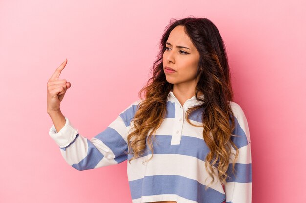 Jonge Mexicaanse vrouw geïsoleerd op roze muur wijzend met vinger naar je alsof uitnodigend dichterbij komen.