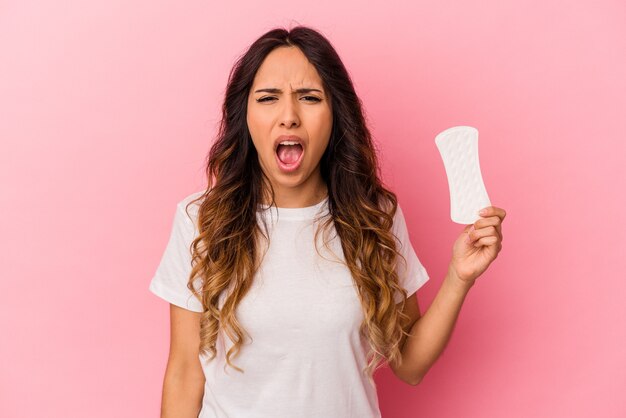 Jonge Mexicaanse vrouw met een kompres geïsoleerd op roze achtergrond schreeuwen erg boos en agressief.