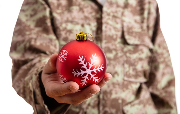 Jonge militair die een rode Kerstmisbal houdt die zich op witte achtergrond bevindt