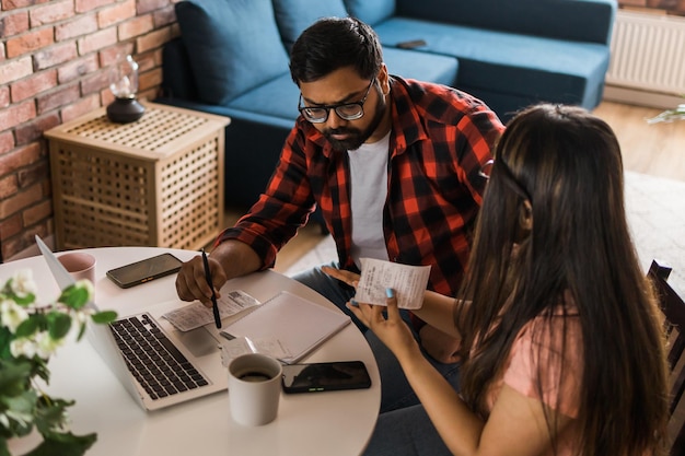 Jonge millennial Indiase man en vrouw die huishoudelijk papierwerk doen, boekhouden en papier herzien