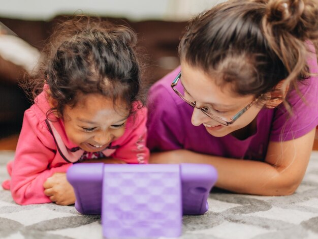Jonge millennial moeder en divers kleutermeisje thuis verlijmen met behulp van tabletcomputer