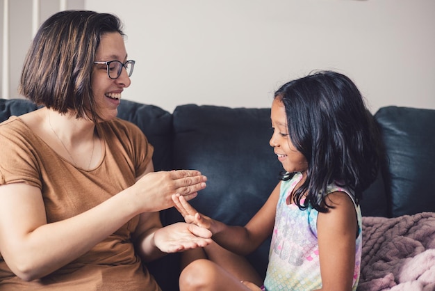 Jonge millennial moeder en dochter thuis spelen met hun handen