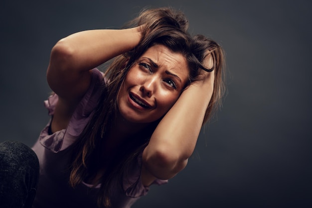 Jonge misbruikte vrouw doodsbang kijkend met armen in haar haar op zoek naar veiligheid.