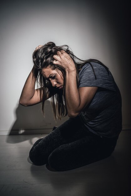 Jonge mishandelde vrouw die gaat zitten en eenzaamheid kijkt met armen in haar haar.
