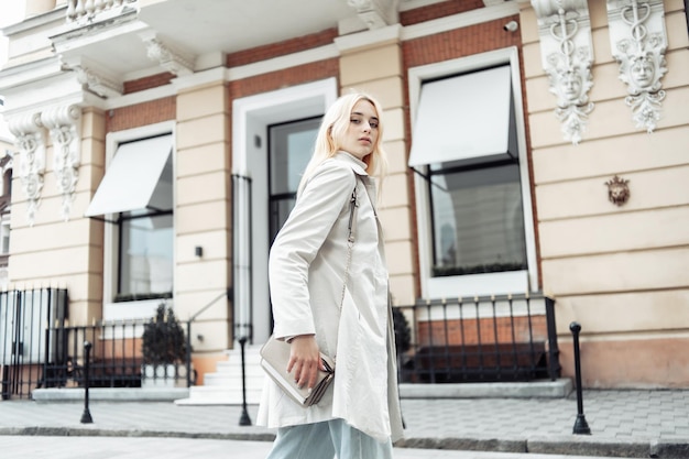 Jonge mode blonde vrouw in een trenchcoat met een tas in de stad