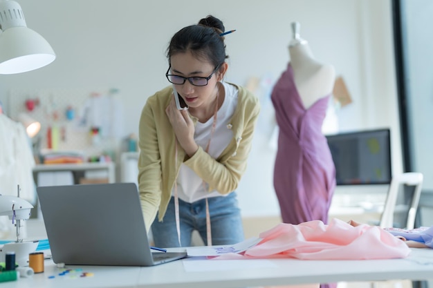 Jonge modeontwerper met een bril die aan de telefoon praat en ontwerpen controleert