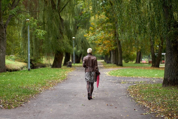 Foto jonge moderne kortharige blonde vrouw die in het herfstpark loopt met een rode paraplu uitzicht vanaf de achterkant