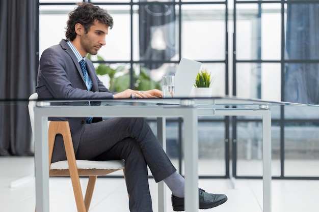 Jonge moderne zakenman aan het werk met behulp van computer terwijl hij op kantoor zit