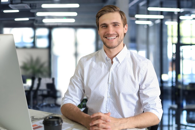 Jonge moderne zakenman aan het werk met behulp van computer terwijl hij op kantoor zit