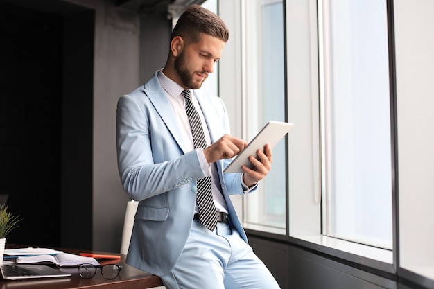 Jonge moderne zakenman aan het werk met behulp van digitale tablet zittend op kantoor.