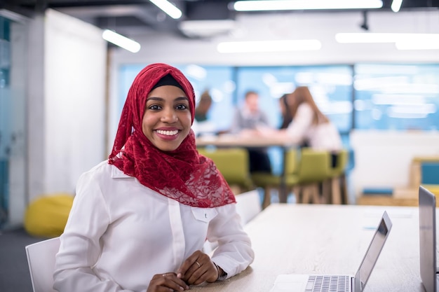 Jonge moderne zwarte moslim zakenvrouw draagt een rode hijab, werken op laptopcomputer in startup office. Diversiteit, multiraciaal concept